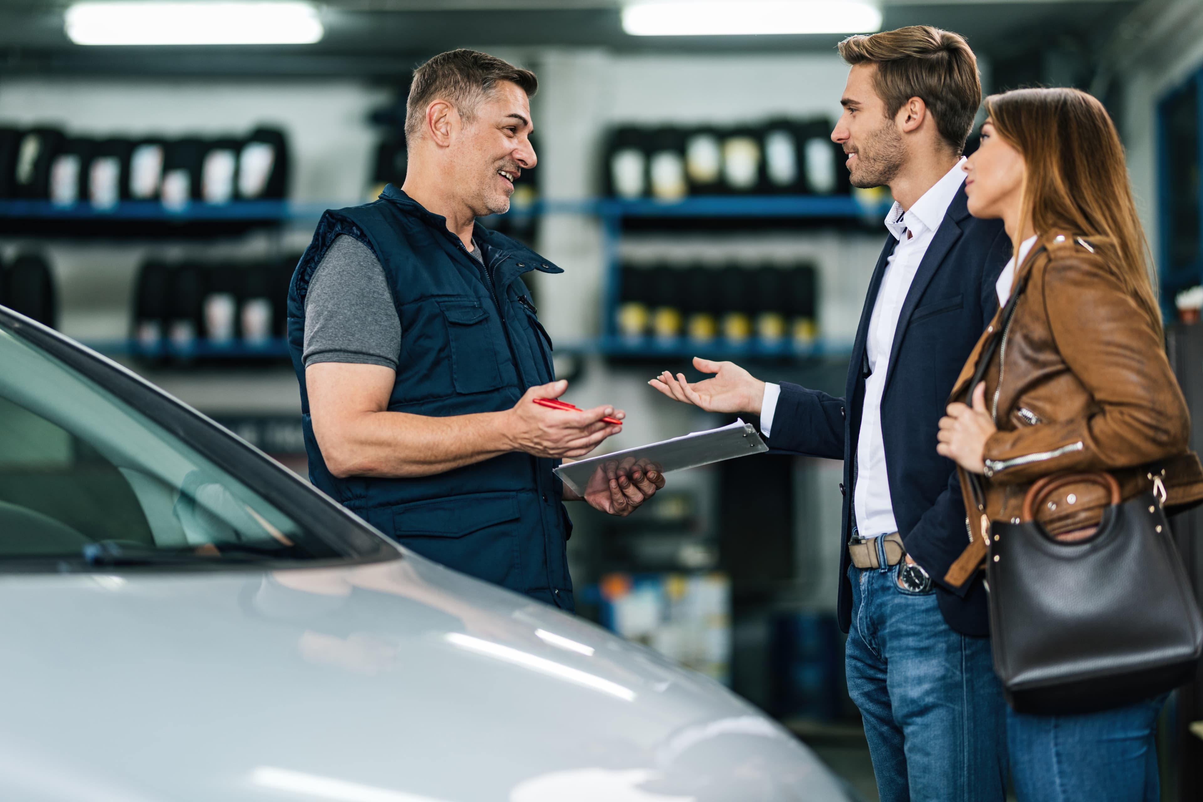 A mechanic explaining an inspection to a couple beside a car